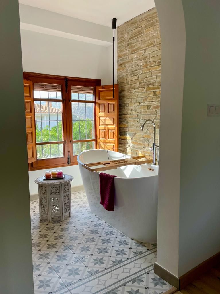 A bathroom with a freestanding bathtub, a wooden vanity, and a stone accent wall.