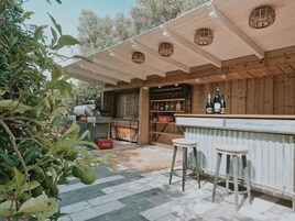 Un área de bar al aire libre con techo de madera, una parrilla y una barra con taburetes.