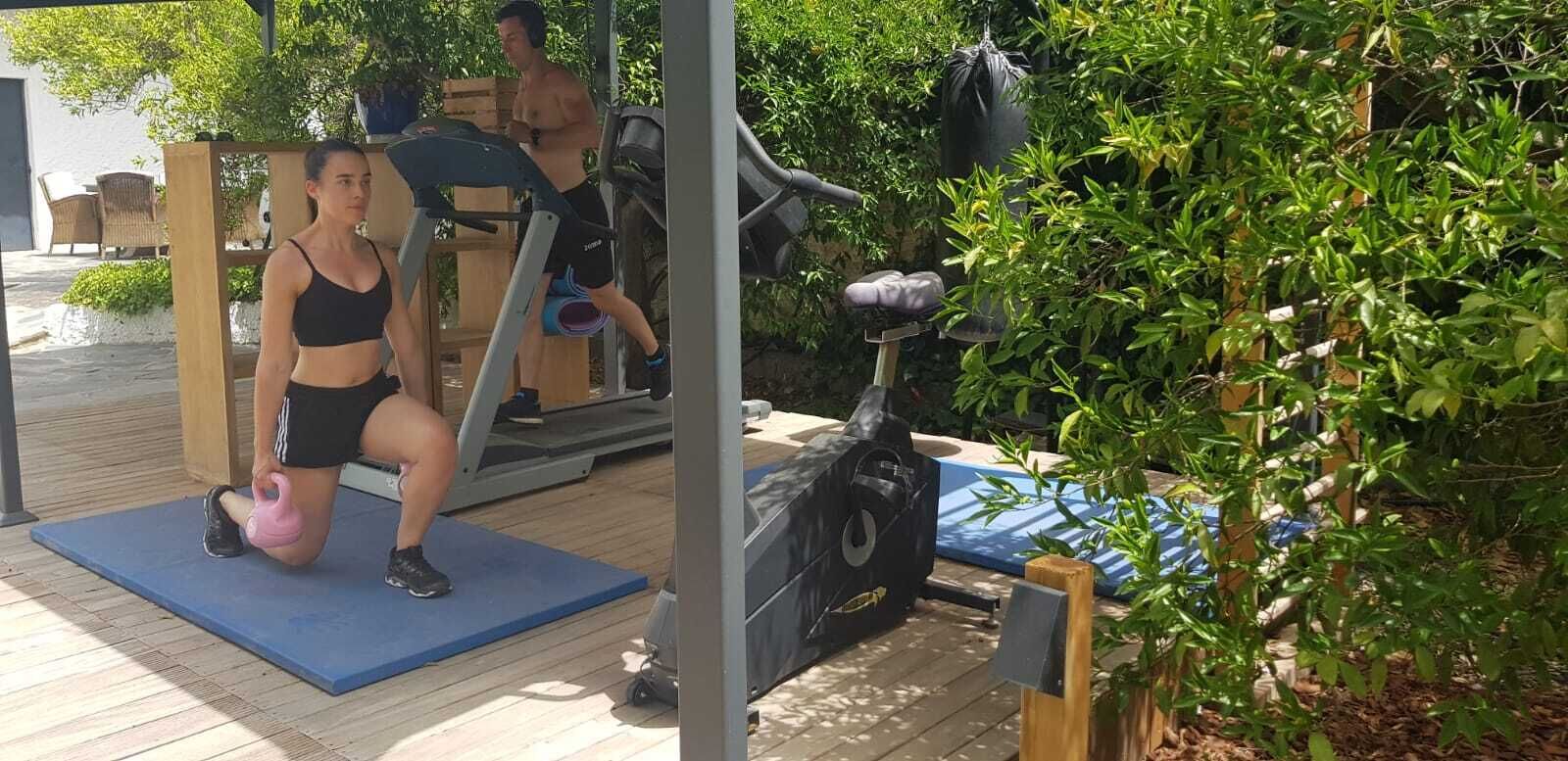 Un espace de remise en forme en plein air équipé d’appareils d’exercice, notamment un tapis de course, un vélo d’appartement et un kettlebell.