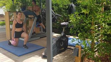 Un espace de remise en forme en plein air équipé d’appareils d’exercice, notamment un tapis de course, un vélo d’appartement et un kettlebell.