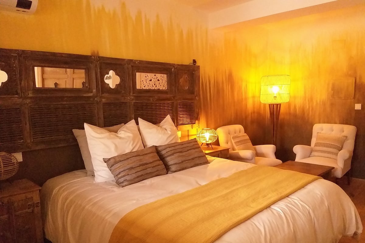 A hotel room with a large bed, two armchairs, a nightstand, and a wall-mounted lamp.