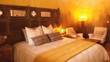 A hotel room with a large bed, two armchairs, a nightstand, and a wall-mounted lamp.