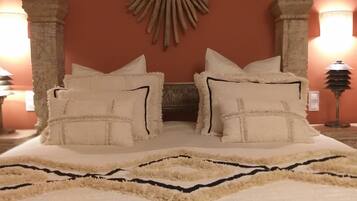 Una cama con múltiples almohadas y un tapete decorativo, iluminada por dos lámparas de pared.