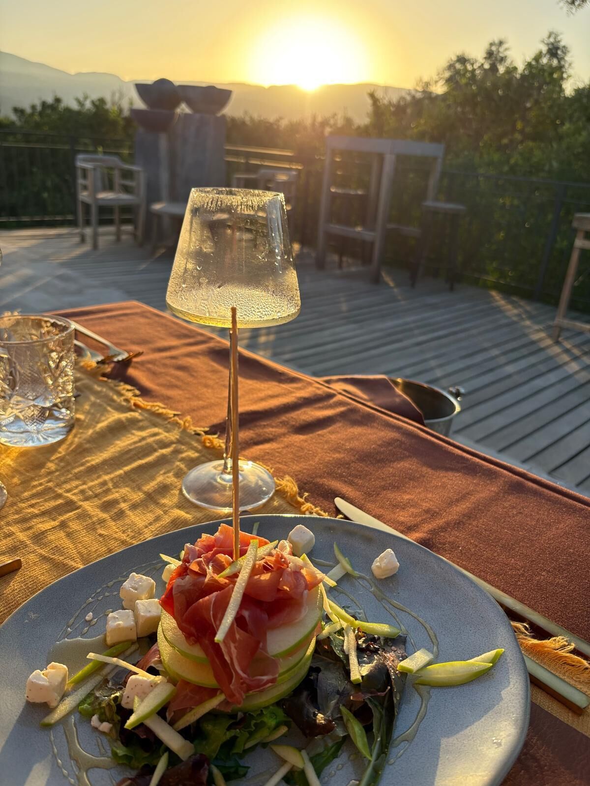 Mesa al aire libre con un plato de comida, un vaso de agua y un vaso de vino.