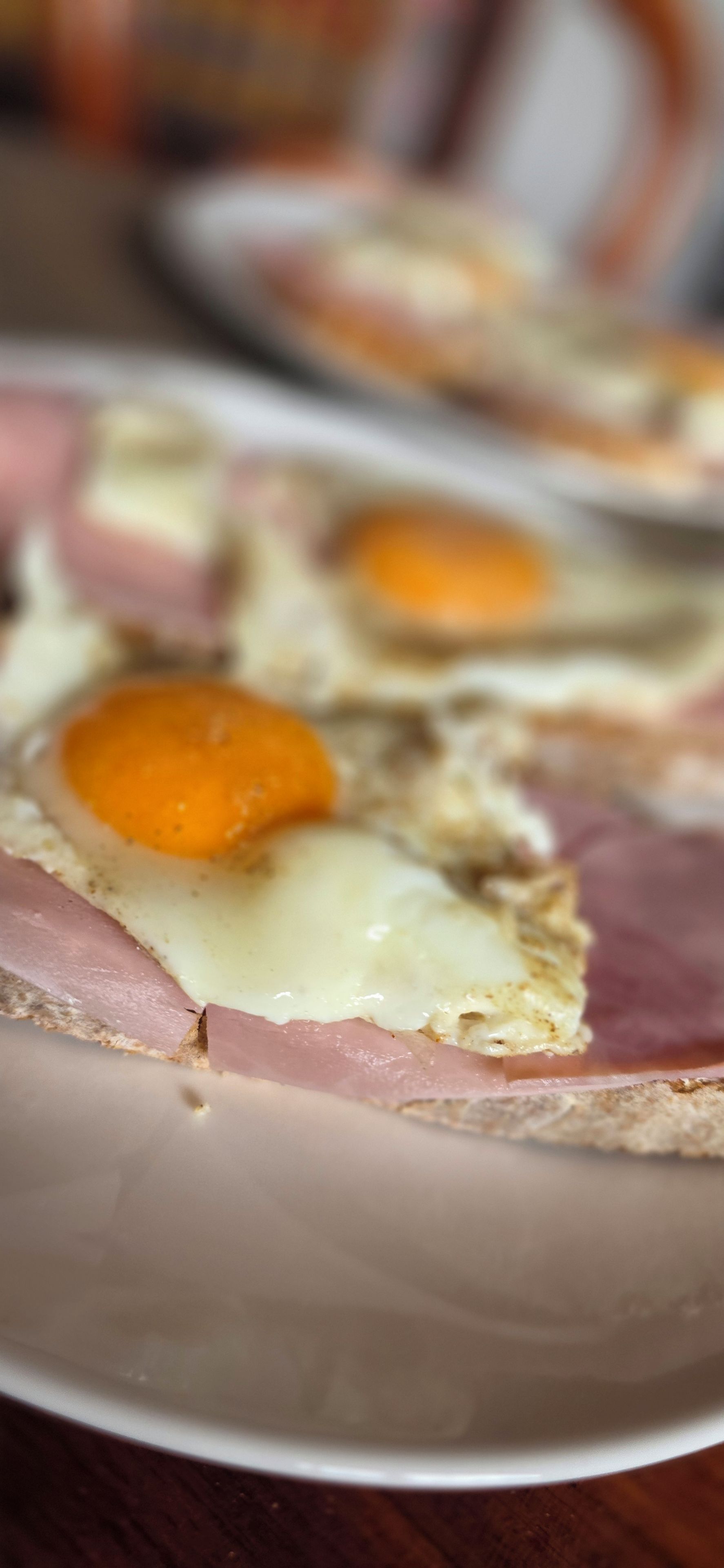 A plate with a sandwich cut in half, containing ham and a fried egg.