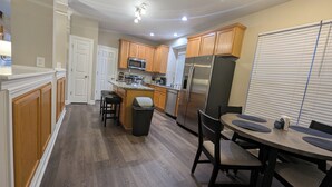 A modern kitchen with wooden cabinets, a stainless steel refrigerator, and a dining area with a round table and chairs. - Cedar's Corner in Concord | Spacious & Clean (Concord)