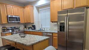 A kitchen with wooden cabinets, a stainless steel refrigerator, a microwave, a coffee maker, and a trash can. - Cedar's Corner in Concord | Spacious & Clean (Concord)