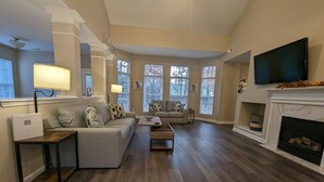 A spacious living room with a high ceiling, hardwood flooring, a fireplace, and a television mounted on the wall. - Cedar's Corner in Concord | Spacious & Clean (Concord)