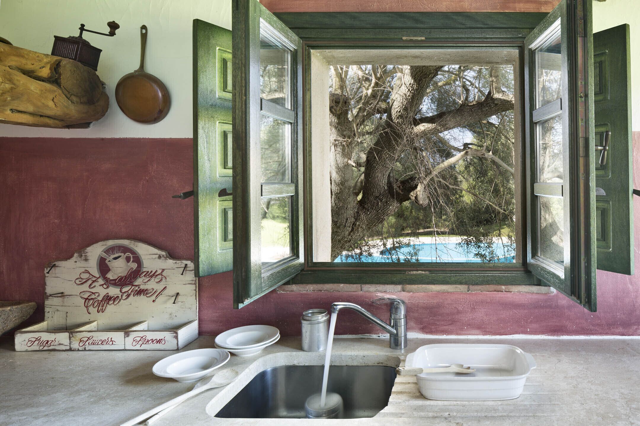 A rustic kitchen with a large window, wooden utensils, and a coffee sign.