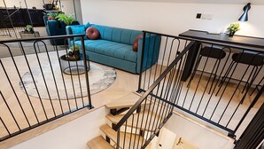 A modern living room with a teal sofa, a coffee table with plants, and a staircase with black railings. - Candy Rose Lux Zagreb Center Apartment (Zagreb)