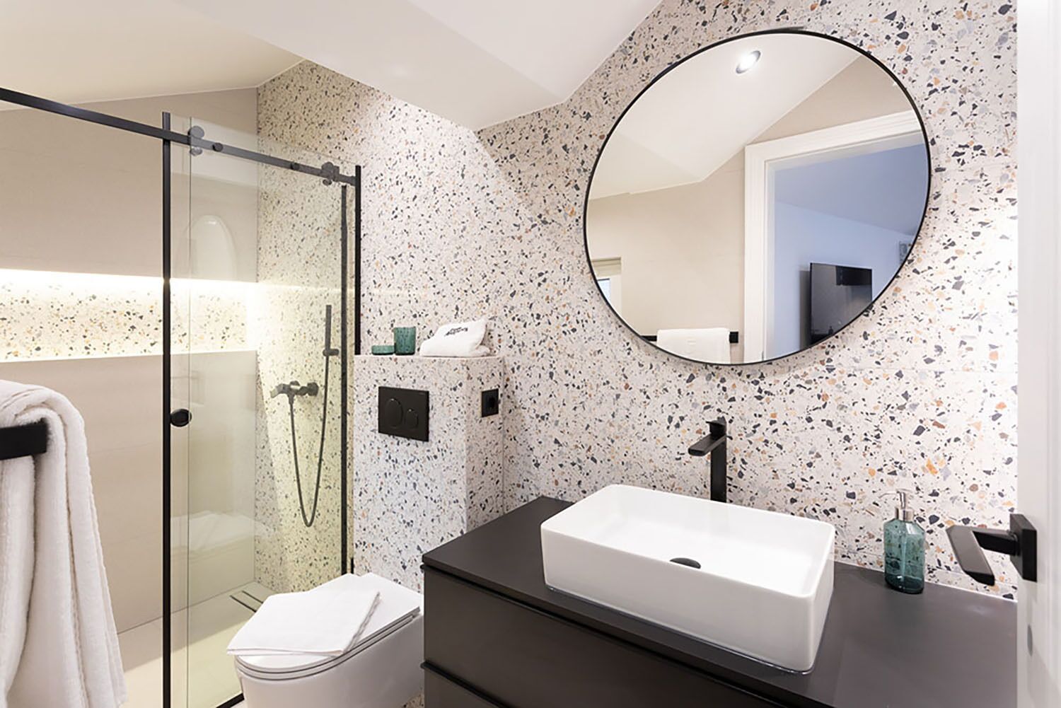Een moderne badkamer met een douchecabine van glas, een wit wastafelmeubel en een ronde spiegel.
