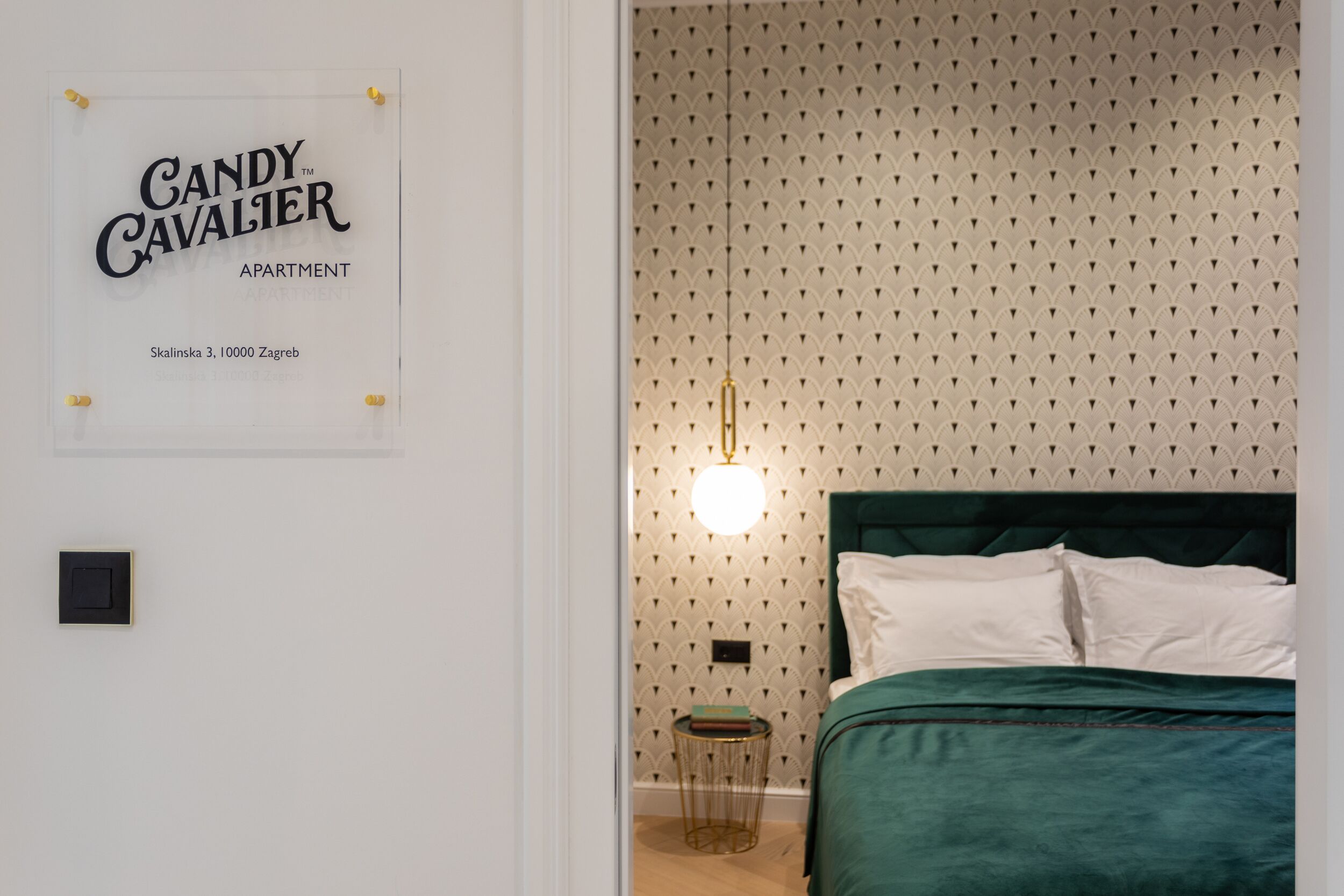A bedroom with a green bed, a wall-mounted light, and a patterned wallpaper.