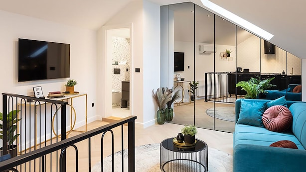 A modern living room with a large flat-screen TV, a blue sofa with decorative pillows, a small round coffee table, and a staircase leading to an upper level. - Candy Rose Lux Zagreb Center Apartment (Zagreb)