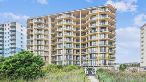 A multi-story residential building with balconies, a central staircase, and a sandy path leading to the entrance. - 10% off 3-7 nights thru Oct. A BEAUTY! Oceanfront 3 bedroom. Sleeps 6. Outdoor pool (North Myrtle Beach)