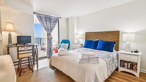 A hotel room with a bed, a desk, a chair, a nightstand with a lamp, and a bookshelf. - 10% off 3-7 nights thru Oct. A BEAUTY! Oceanfront 3 bedroom. Sleeps 6. Outdoor pool (North Myrtle Beach)