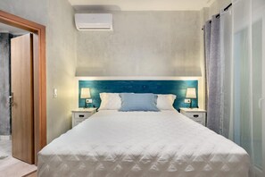 A hotel room with a bed, two bedside tables with lamps, a wall-mounted air conditioner, and a door. - Diogenis Villa Kefalonia (Kefalonia)