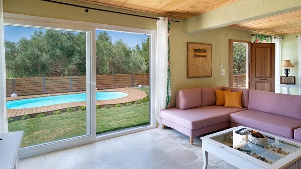 Un vaste salon doté d’une grande porte-fenêtre coulissante donnant sur une piscine, d’un canapé rose et d’une table basse en verre.