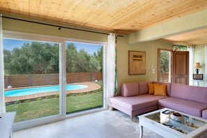 A spacious living room with a large sliding glass door leading to a pool area, a pink sofa, and a glass coffee table.