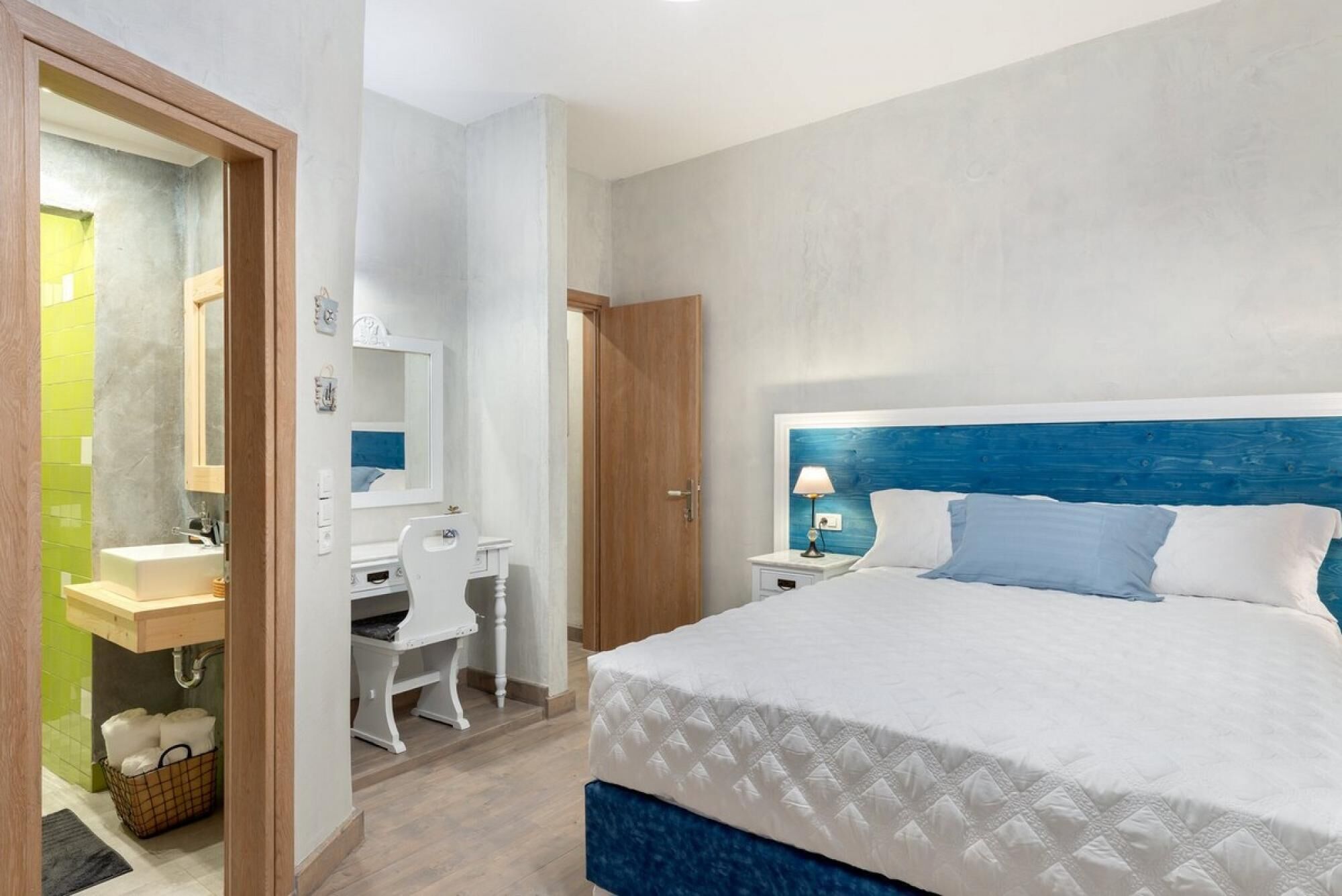 A bedroom with a bed, bedside table, lamp, and a desk with chair and mirror.