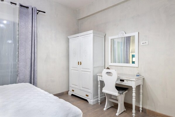 A bedroom with a bed, a wardrobe, a desk with a chair, and a mirror.