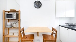 Una cocina con una mesa de madera, dos sillas, un microondas, un reloj y armarios blancos.