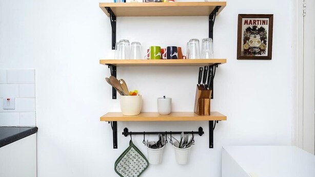 Een keuken met drie houten planken, een hangende pannendroger en een lijst met een foto aan de muur.