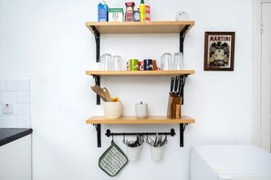A kitchen with three wooden shelves, a hanging pot rack, and a framed picture on the wall. - Lovely Top Floor Flat in Vibrant New Cross London (Greater London)