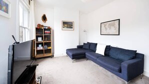 Een woonkamer met een donkerblauwe modulaire bank, een flatscreen televisie, een houten boekenkast en een wereldbol als wanddecoratie.
