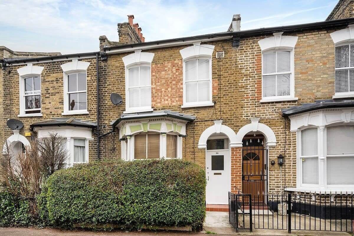 A row of terraced houses with white-framed windows, a brick facade, and a black metal fence in front.