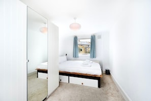 A bedroom with a bed, bedside tables, a window with curtains, a radiator, and a door leading to another room. - Lovely Top Floor Flat in Vibrant New Cross London (Greater London)