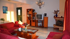 A living room with red sofas, a coffee table, a bookshelf, a television, and a fireplace. - Villa Fantasia Kefalonia (Kefalonia)