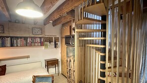 A cozy room with a wooden ceiling, a round table with a chessboard, a chair, a bookshelf, and a decorative wooden partition.