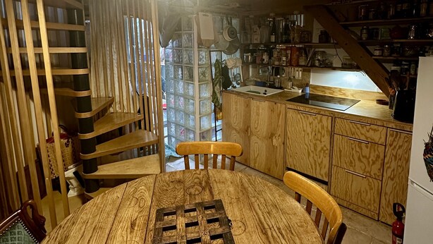 A wooden dining table with chairs, a kitchen area with wooden cabinets, and a staircase.