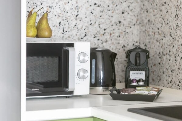 Una cocina equipada con microondas, cafetera y una caja de té.