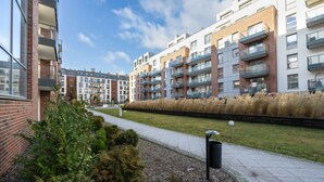 Un moderno complejo de apartamentos con varios balcones, un jardín ajardinado y un cielo despejado.