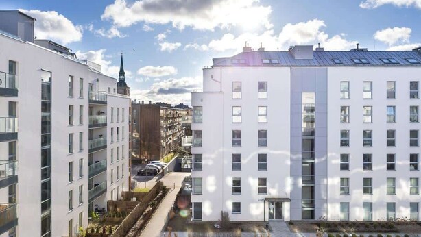 Un moderno edificio de apartamentos con varios pisos, ventanas amplias y un cielo despejado.