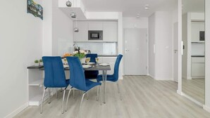 A modern kitchen with white cabinets, a microwave, and a dining area with blue chairs and a table set for two.