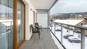 A balcony with a table and chairs, a view of a snowy landscape, and a building in the background.