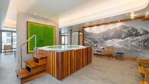 A modern lobby with a wooden reception desk, a glass-topped hot tub, and a mural of a mountainous landscape.