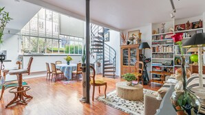 A spacious living room with a dining area, a spiral staircase, and a large bookshelf filled with books and decorative items. - Gorgeous home in Paris with WiFi (Paris)
