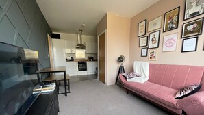 A modern living room with a pink sofa, a flat-screen TV, and a dining area with a table and chairs. - Stylish 1-bed Apartment in Swindon (Swindon)