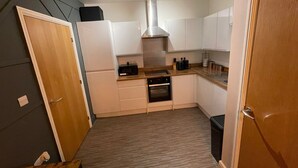 A compact kitchen with white cabinets, a microwave, a stove, and a ventilation hood. - Stylish 1-bed Apartment in Swindon (Swindon)