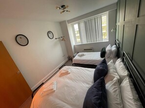 A bedroom with two beds, a window with blinds, a ceiling fan, and a wall clock. - Stylish 1-bed Apartment in Swindon (Swindon)