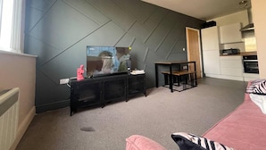 A modern living room with a large flat-screen TV, a small table, and a sofa. - Stylish 1-bed Apartment in Swindon (Swindon)