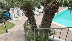 A poolside area with a stone patio, white lounge chairs, and palm trees. - Holiday home with private pool and sea view (Punta de Su Turrione)