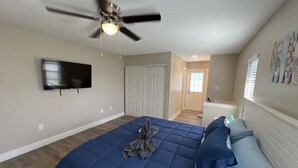 Un dormitorio con cama, ventilador de techo, televisión y una puerta que da a otra habitación.