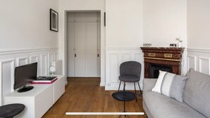 A living room with a fireplace, a grey sofa, a small table, and a TV on a white cabinet. - Seb's Place Montmartre | Paris Safe and quiet area (Paris)