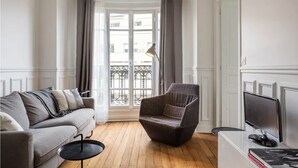 A living room with a grey sofa, a dark armchair, a small round table, and a TV on a stand. - Seb's Place Montmartre | Paris Safe and quiet area (Paris)