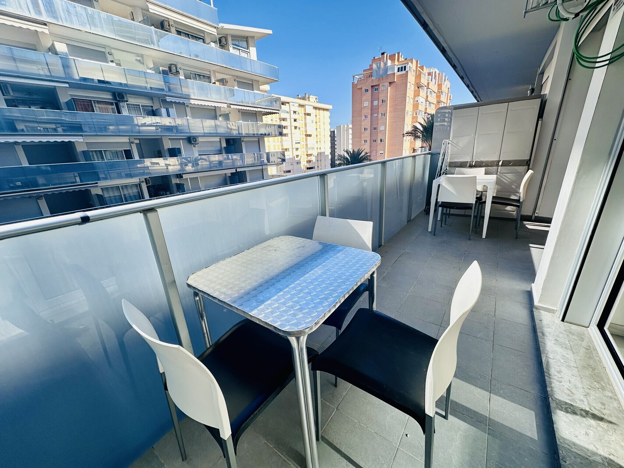 A balcony with a table and chairs, overlooking a cityscape with buildings.