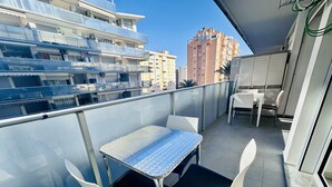 A balcony with a table and chairs, overlooking a cityscape with buildings.